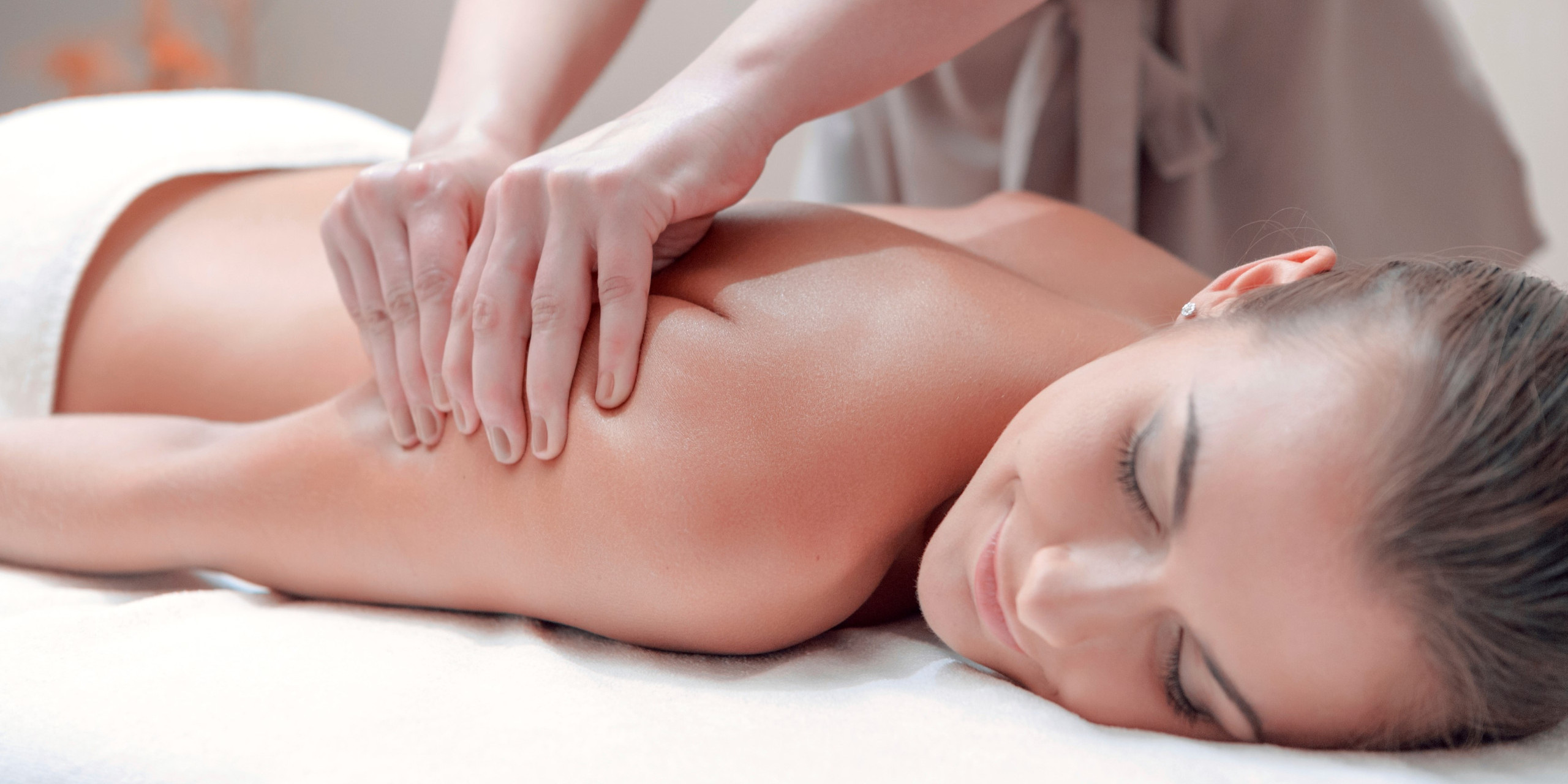 Eine Person erhält eine entspannende Rückenmassage in einem hellen Raum. Die Massagetherapeutin übt sanften Druck auf den Rücken der liegenden Person aus, die entspannt wirkt.